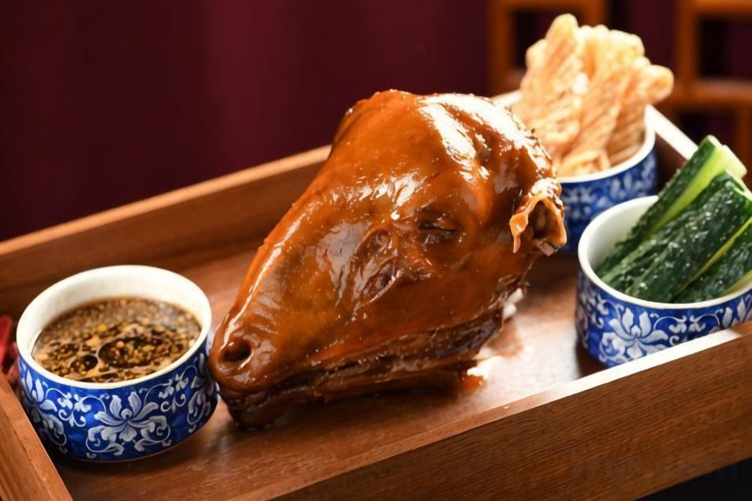 Un cochon rôti, présenté sur un plateau en bois, accompagné de deux petits bols de sauce et de légumes marinés.