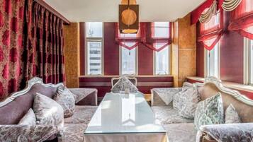 Una habitación con una mesa de vidrio, sofás estampados y cortinas rojas.