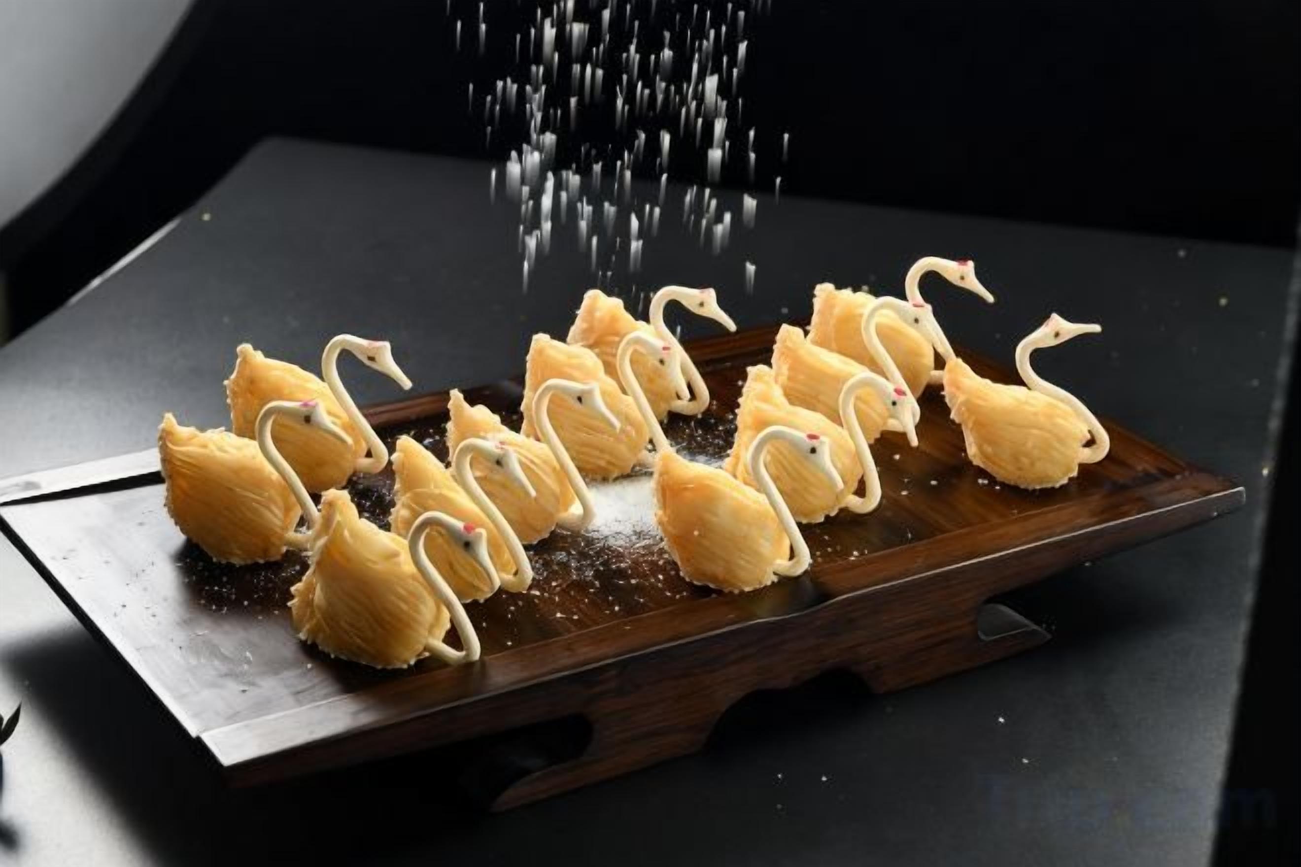 Bandeja de pasteles con forma de cisne sobre una tabla de madera, espolvoreados con azúcar.