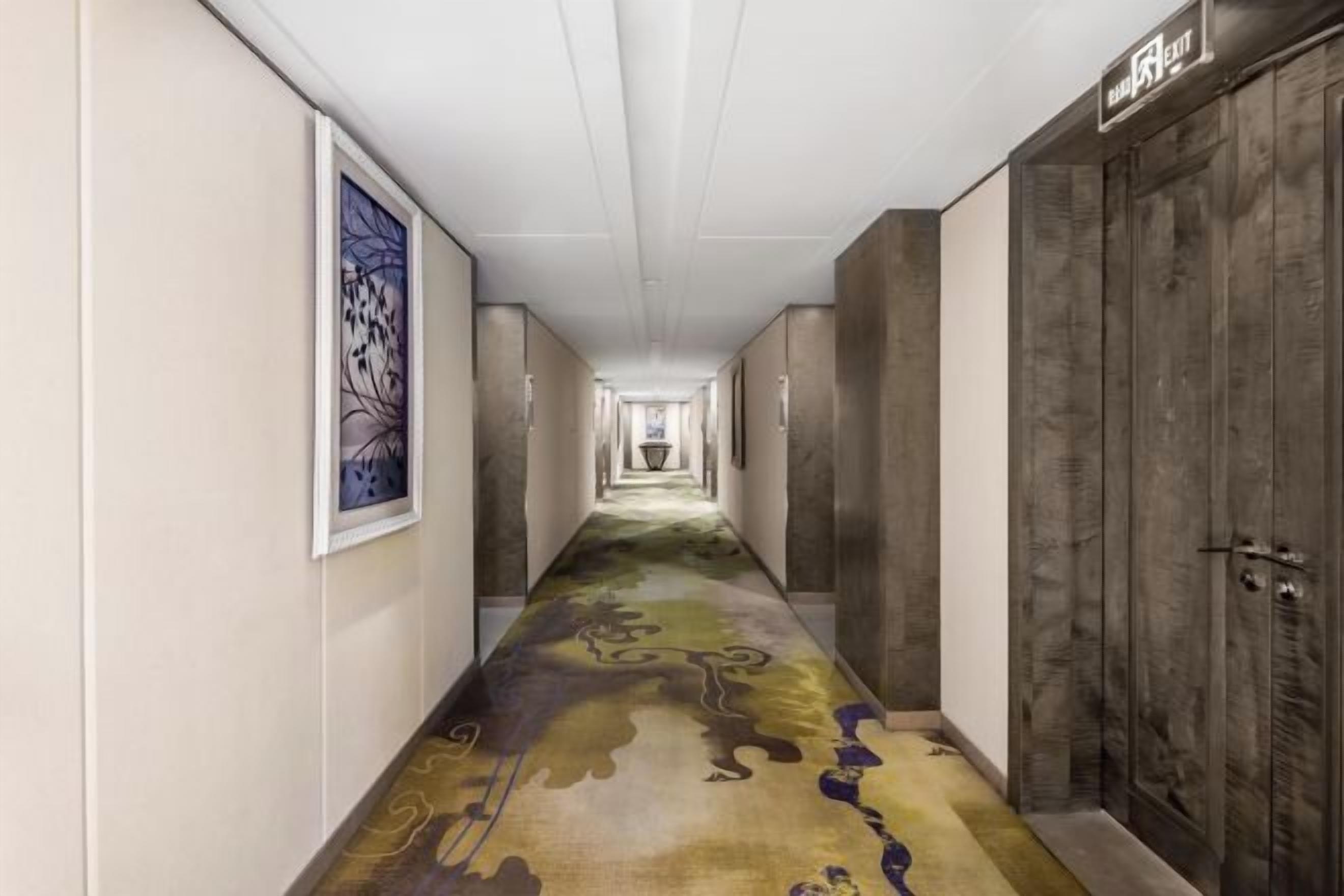 A hotel corridor with a patterned carpet, framed artwork on the walls, and wooden doors.
