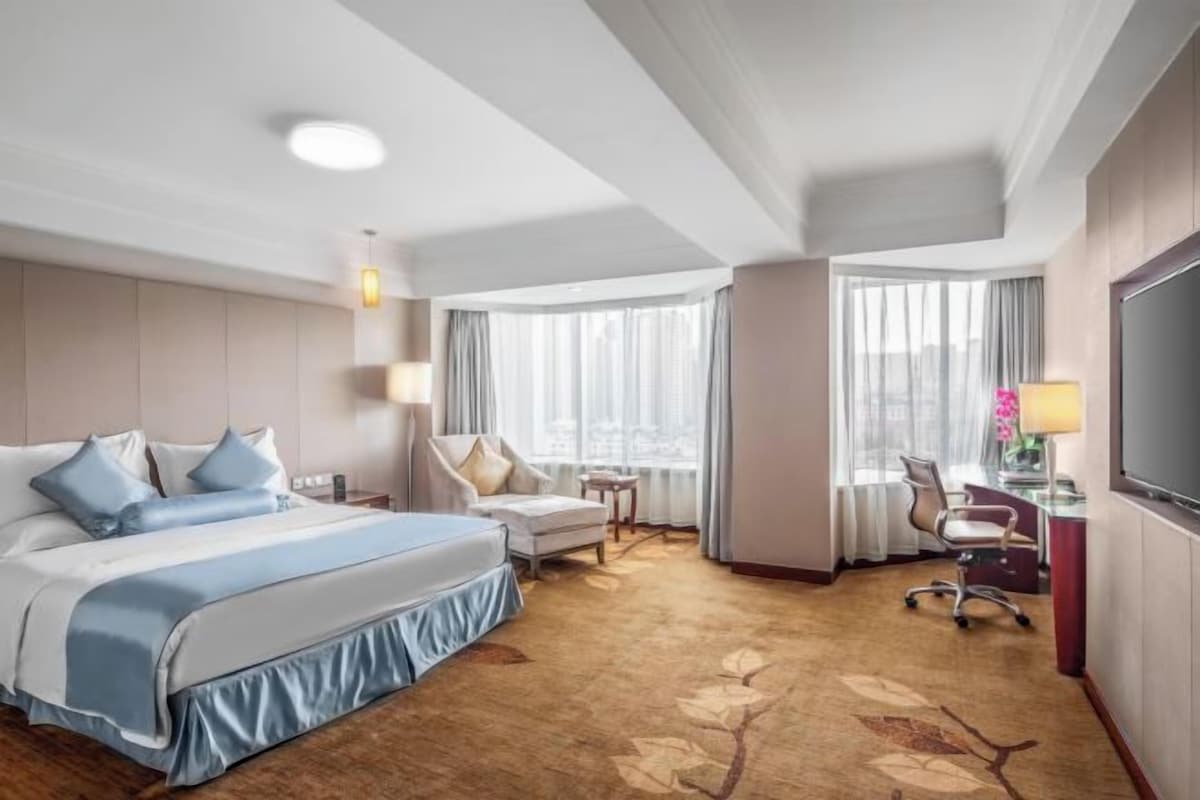 A hotel room with a large bed, a desk, a chair, and a TV.