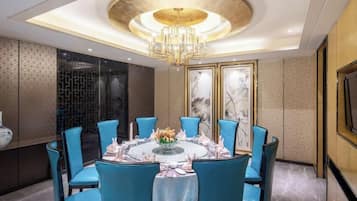 A dining room with a round table, blue chairs, and a chandelier.