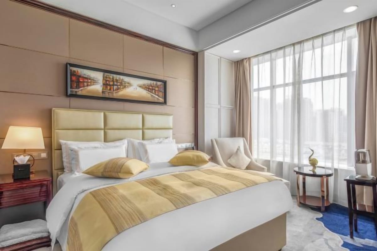 A hotel room with a large bed, a chair, a nightstand, and a window with curtains.