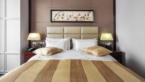 Quarto de hotel com uma cama grande, duas mesas de cabeceira com luminárias, uma cabeceira e uma obra de arte emoldurada acima da cama.
