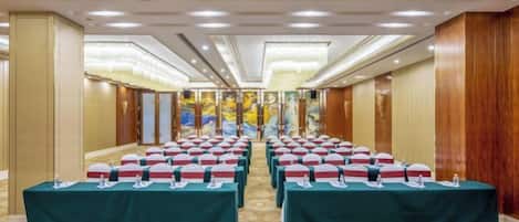 Un salón de conferencias con filas de mesas, cada una con un micrófono y una botella de agua.