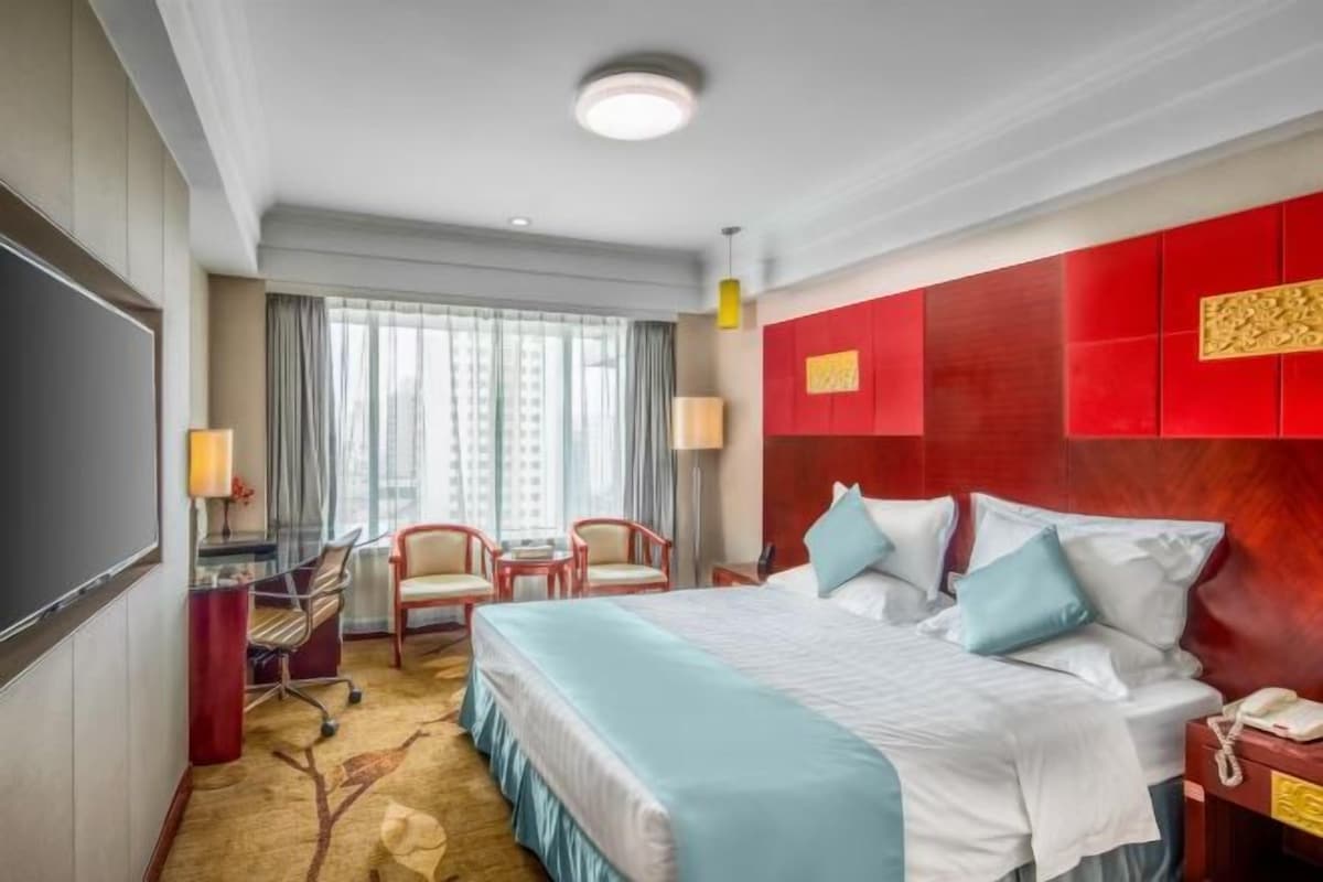 A hotel room with a large bed, a desk with a chair, a TV, and a window with curtains.