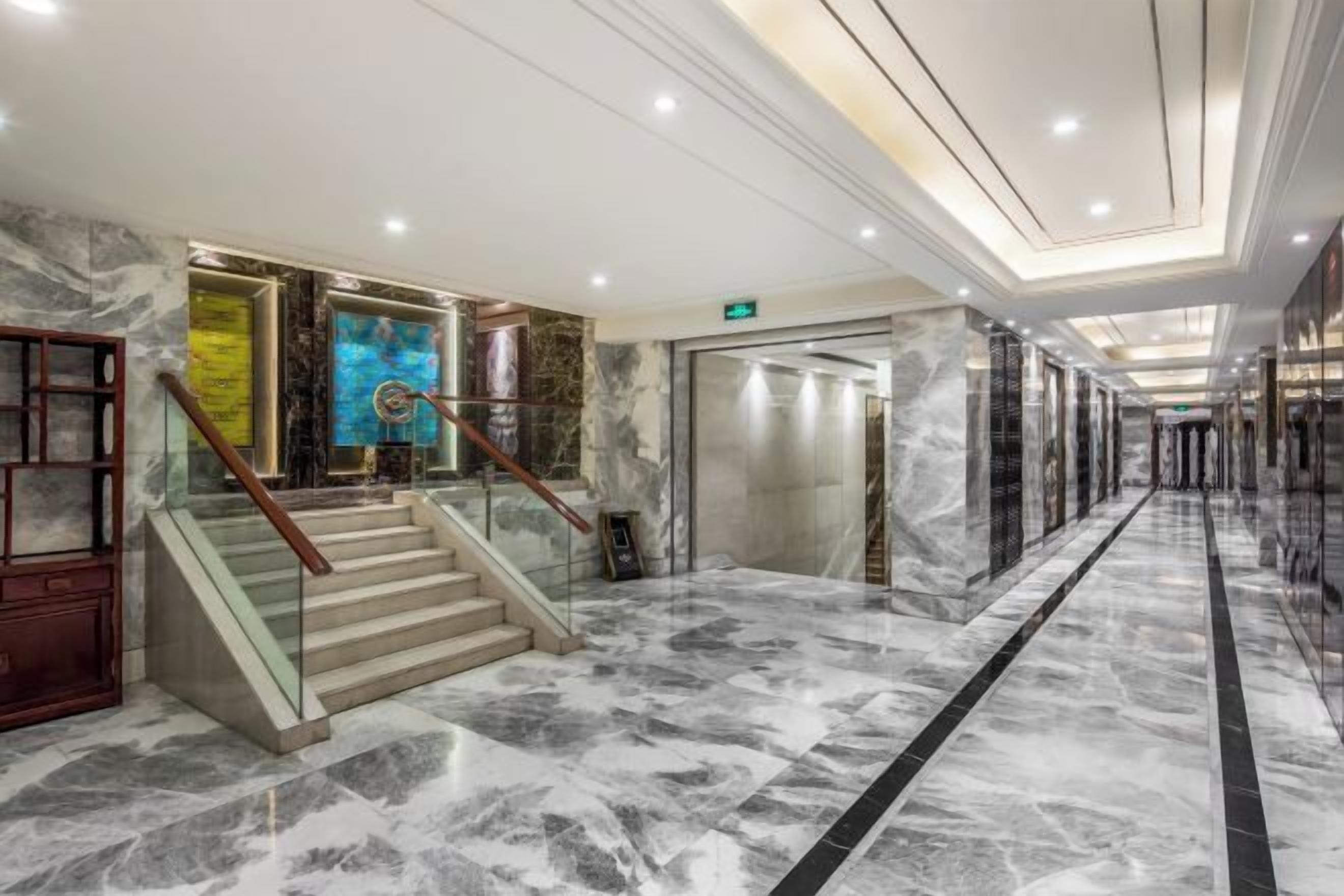 Un hall d’hôtel doté d’un sol en marbre, d’un escalier avec des rampes en verre et d’un design de plafond moderne.