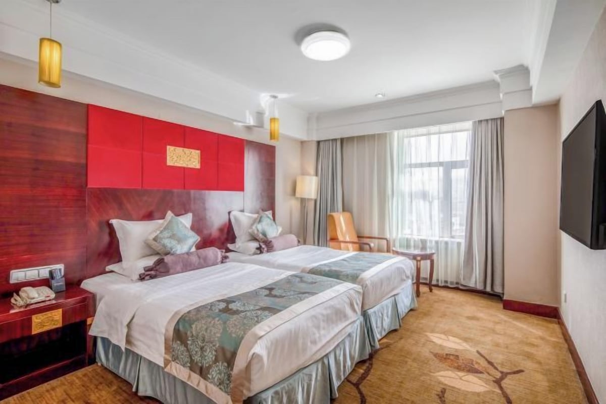 A hotel room with two beds, a TV, a desk, and a chair.