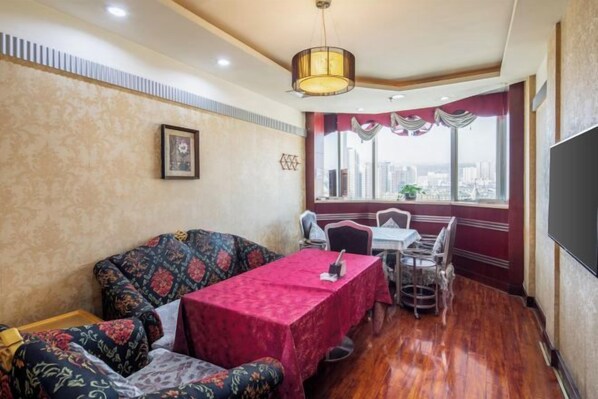 A room with a dining table, chairs, a sofa, a television, and a window with a city view.