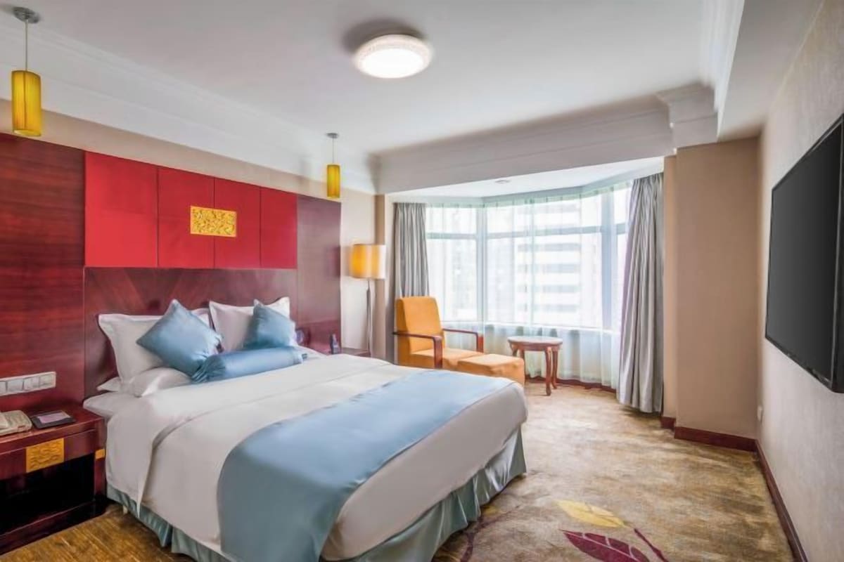 A hotel room with a large bed, a desk, a chair, a TV, and a window with curtains.