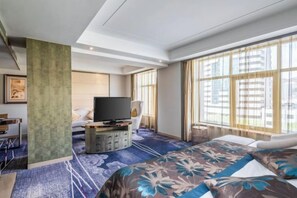 A hotel room with a large bed, a television, a desk, and a window with curtains.