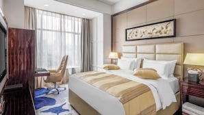 Quarto de hotel com cama grande, escrivaninha, cadeira, televisão e janela com cortinas.