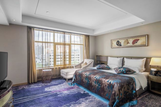 Habitación de hotel con una cama grande, una silla, un televisor y una ventana con cortinas.