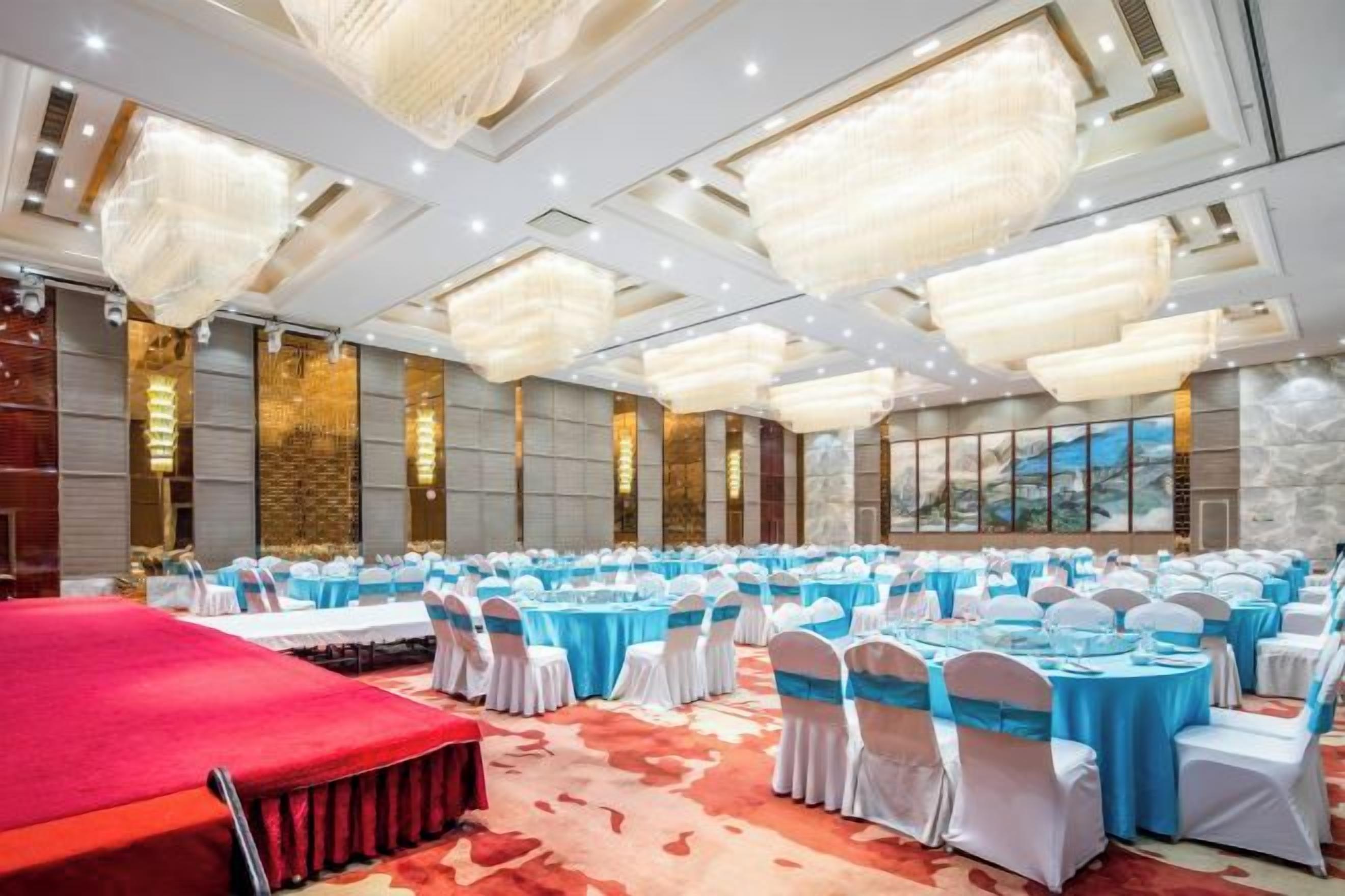 A banquet hall with round tables, white chairs, and a red carpet.