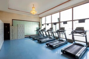 Un gimnasio con cintas de correr alineadas a lo largo de una pared, ventanas amplias y una lámpara de araña.