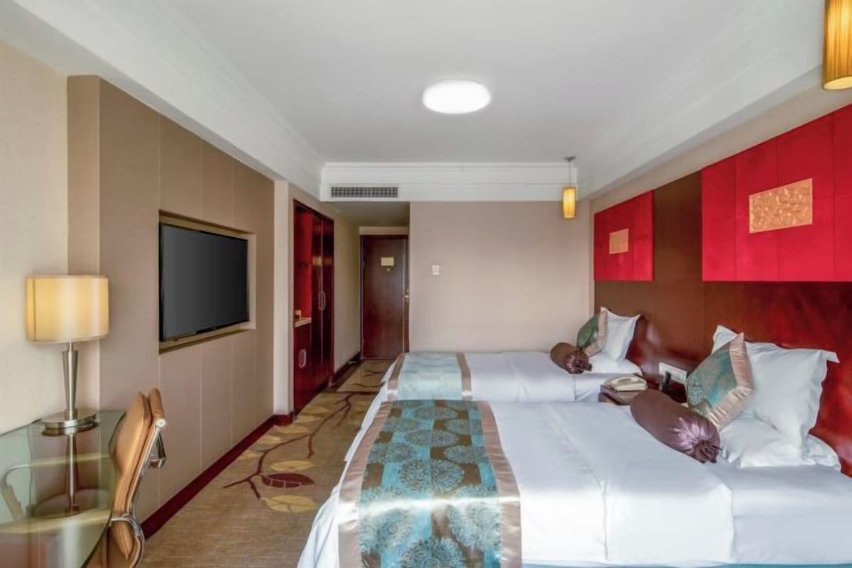 A hotel room with a large bed, a television, a desk with a lamp, and a red accent wall.