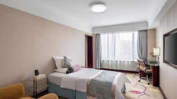 Una habitación de hotel con cama, escritorio, silla, televisor y ventana con cortinas.