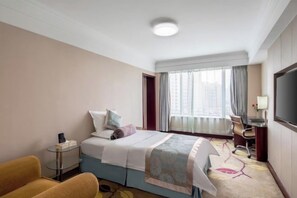 Una habitación de hotel con cama, escritorio, silla, televisor y ventana con cortinas.