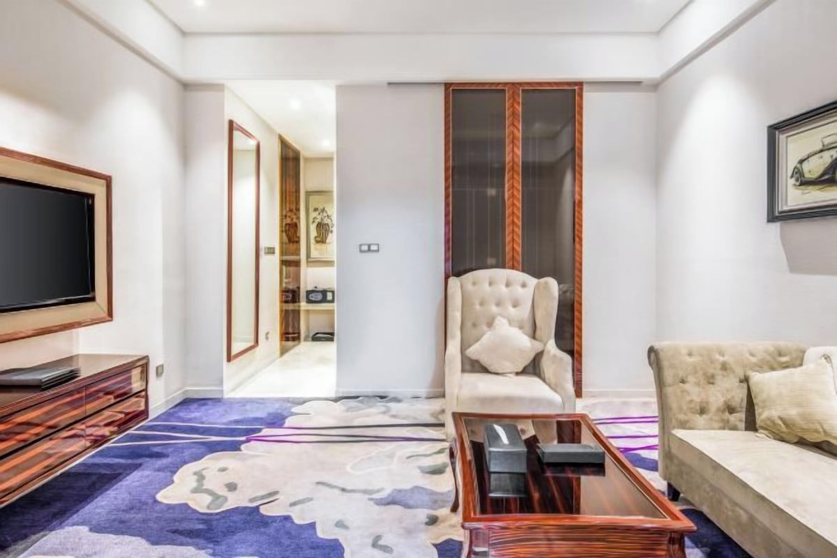 A living room with a flat-screen TV, a sofa, a coffee table, and a patterned carpet.