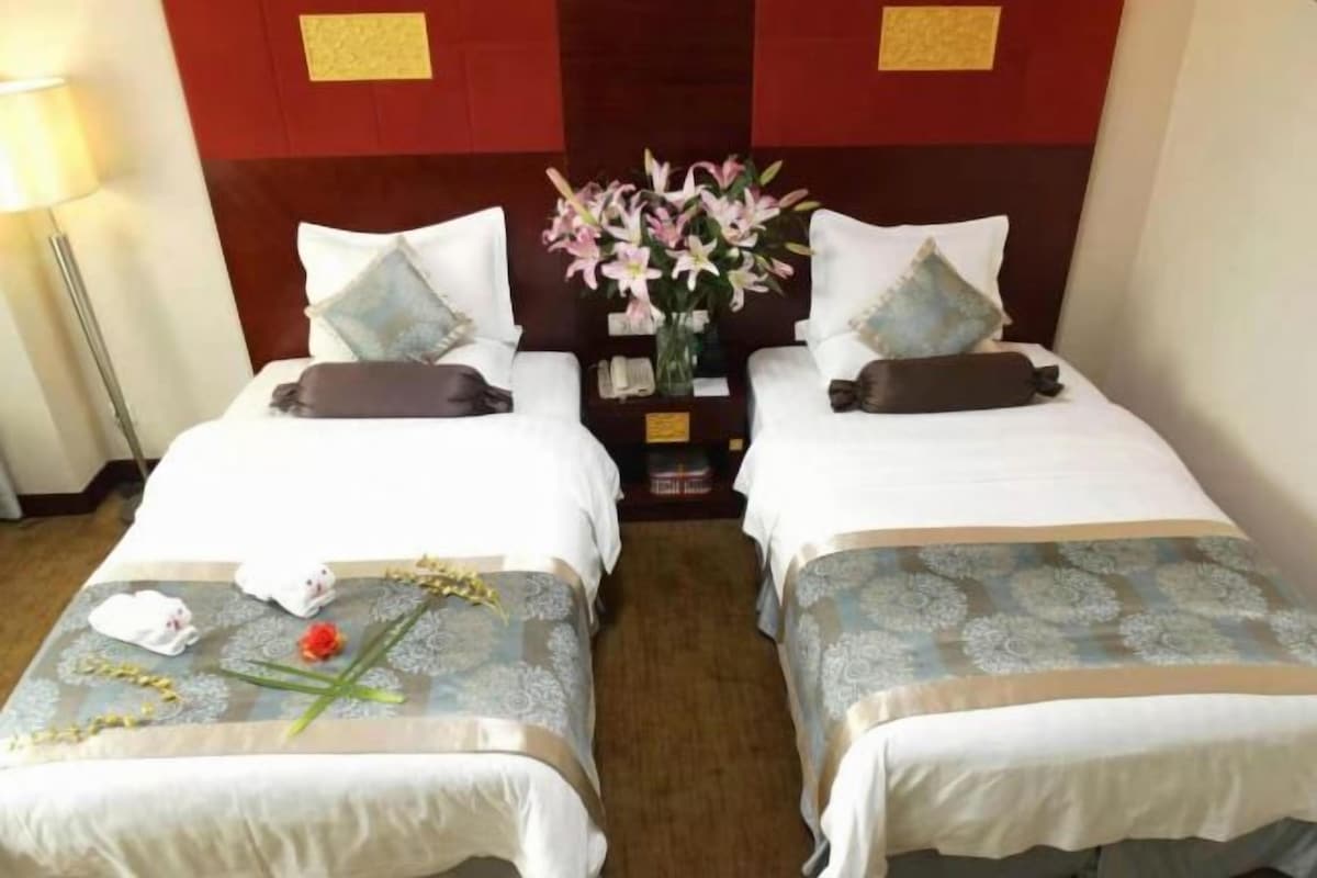 A hotel room with two beds, each with a pillow, a vase of flowers, and a small table between them.