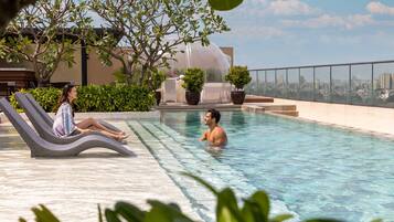 A rooftop pool with lounge chairs, a clear view of the cityscape, and potted plants.
