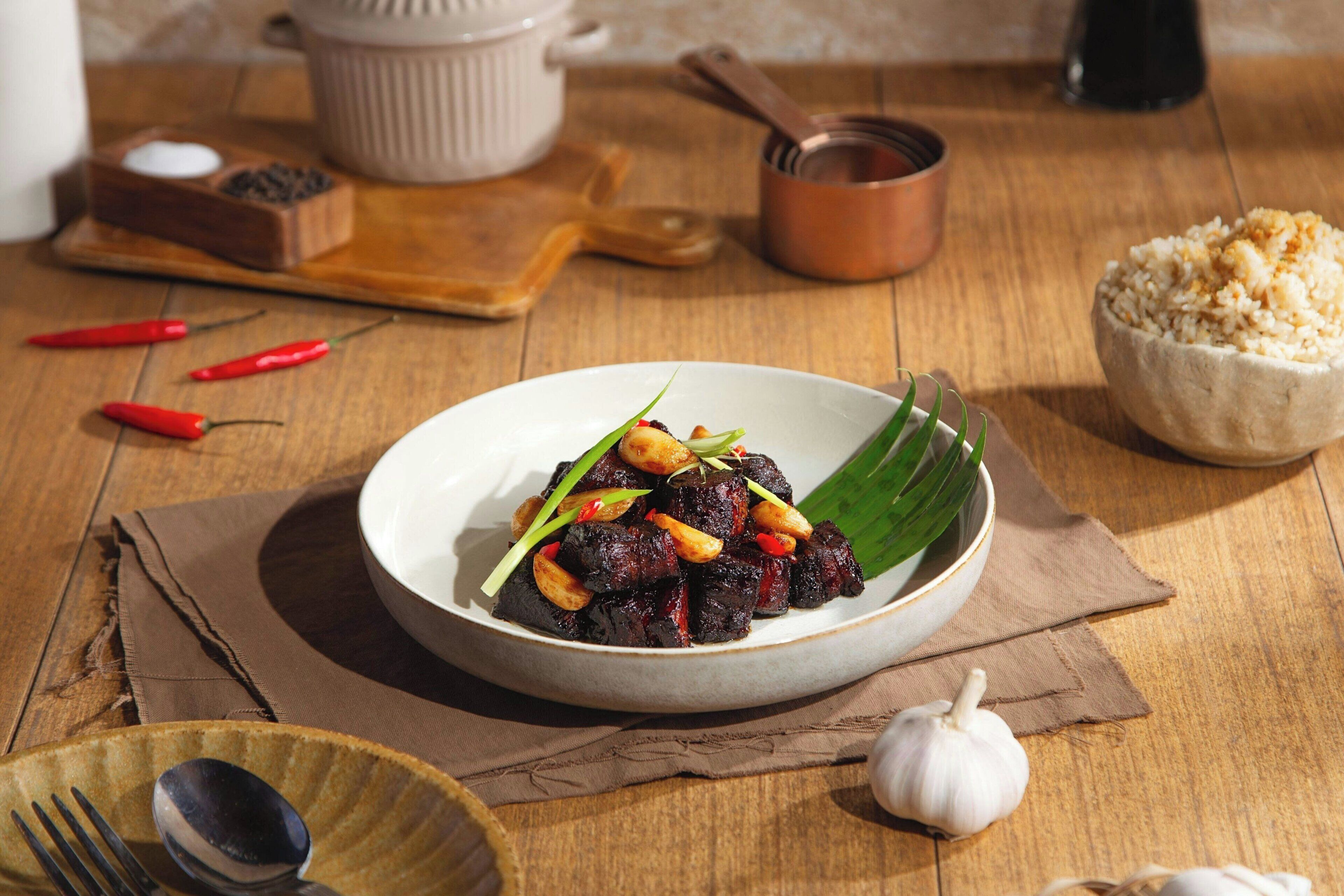 A plate of food with a bowl of rice and a spoon on a wooden table.