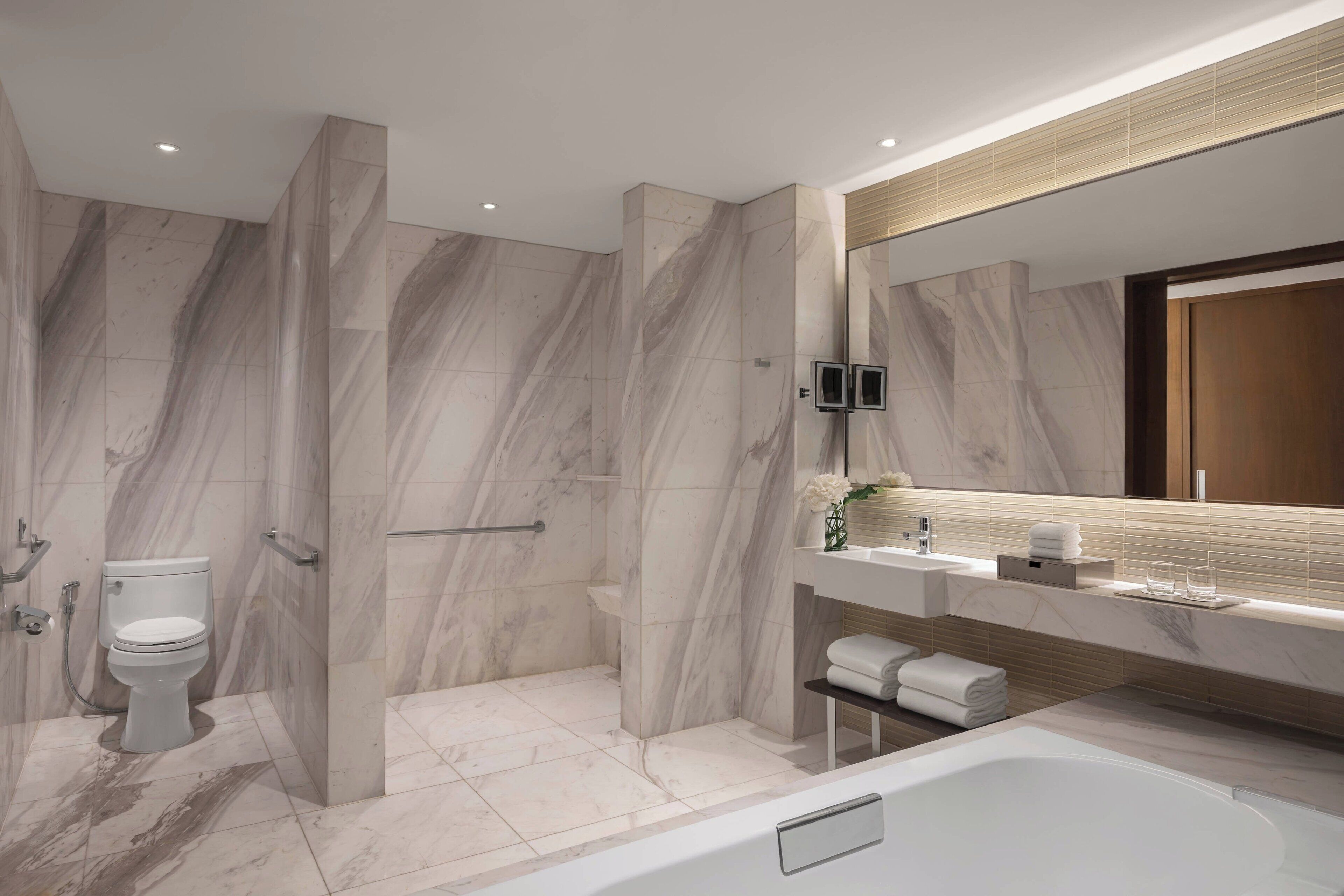 A modern bathroom with a marble floor, a bathtub, a toilet, and a shower area.