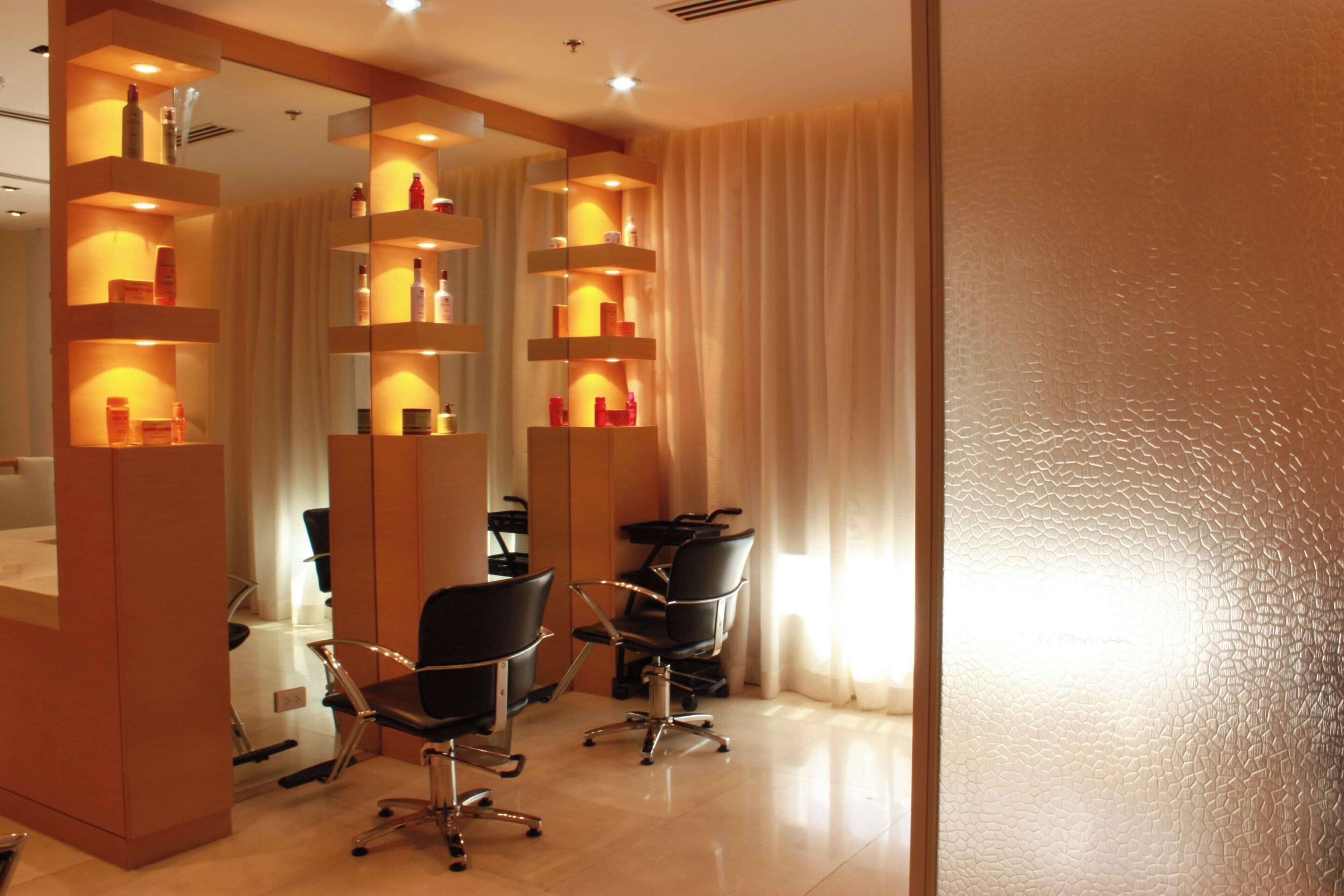 Un salón de belleza moderno con dos sillas negras, paredes espejadas y estantes con productos para el cabello.