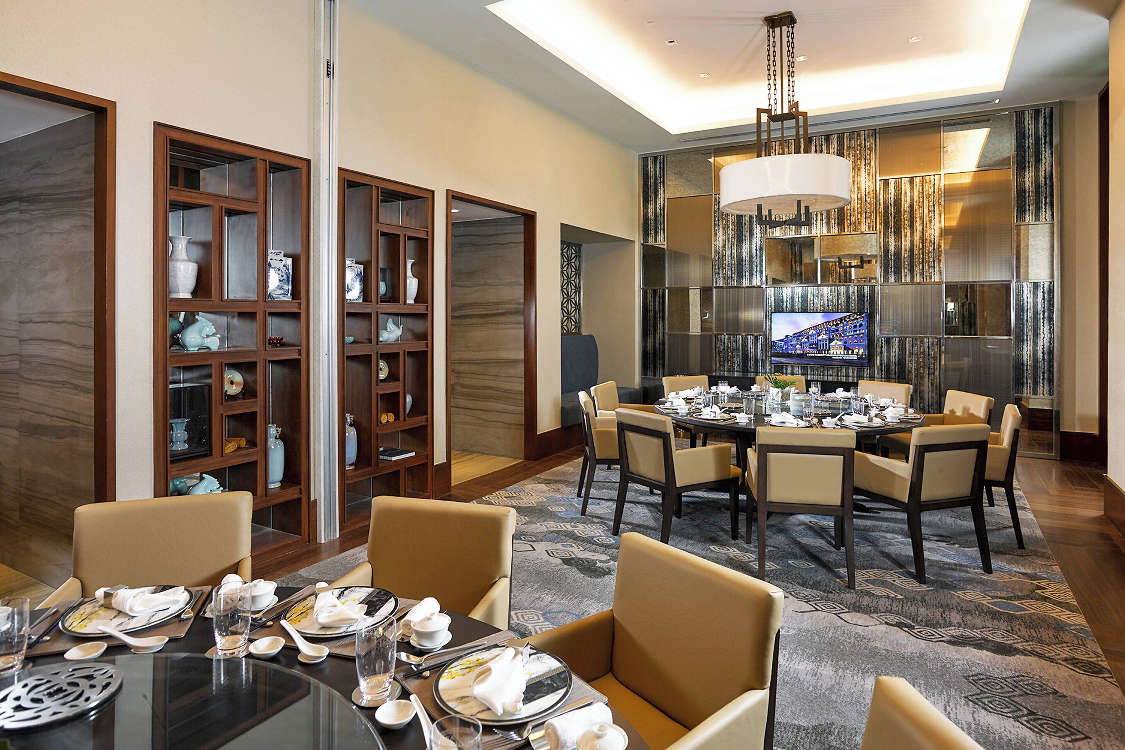 A dining area with a round table set for six, surrounded by six chairs. There are two wooden display cabinets with glass doors on either side of the room.