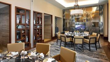 A dining area with a round table set for six, surrounded by six chairs. There are two wooden display cabinets with glass doors on either side of the room.