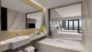 A modern bathroom with a large mirror, two sinks, a bathtub, and a view of a bedroom with a cityscape.