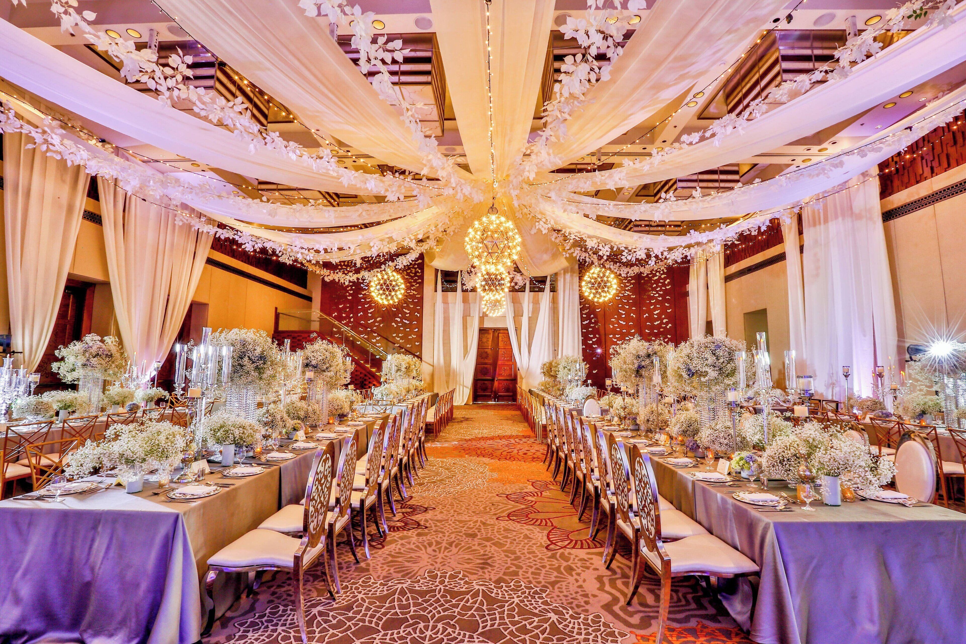 A banquet hall with long tables set for a formal event, draped with white fabric and floral arrangements.