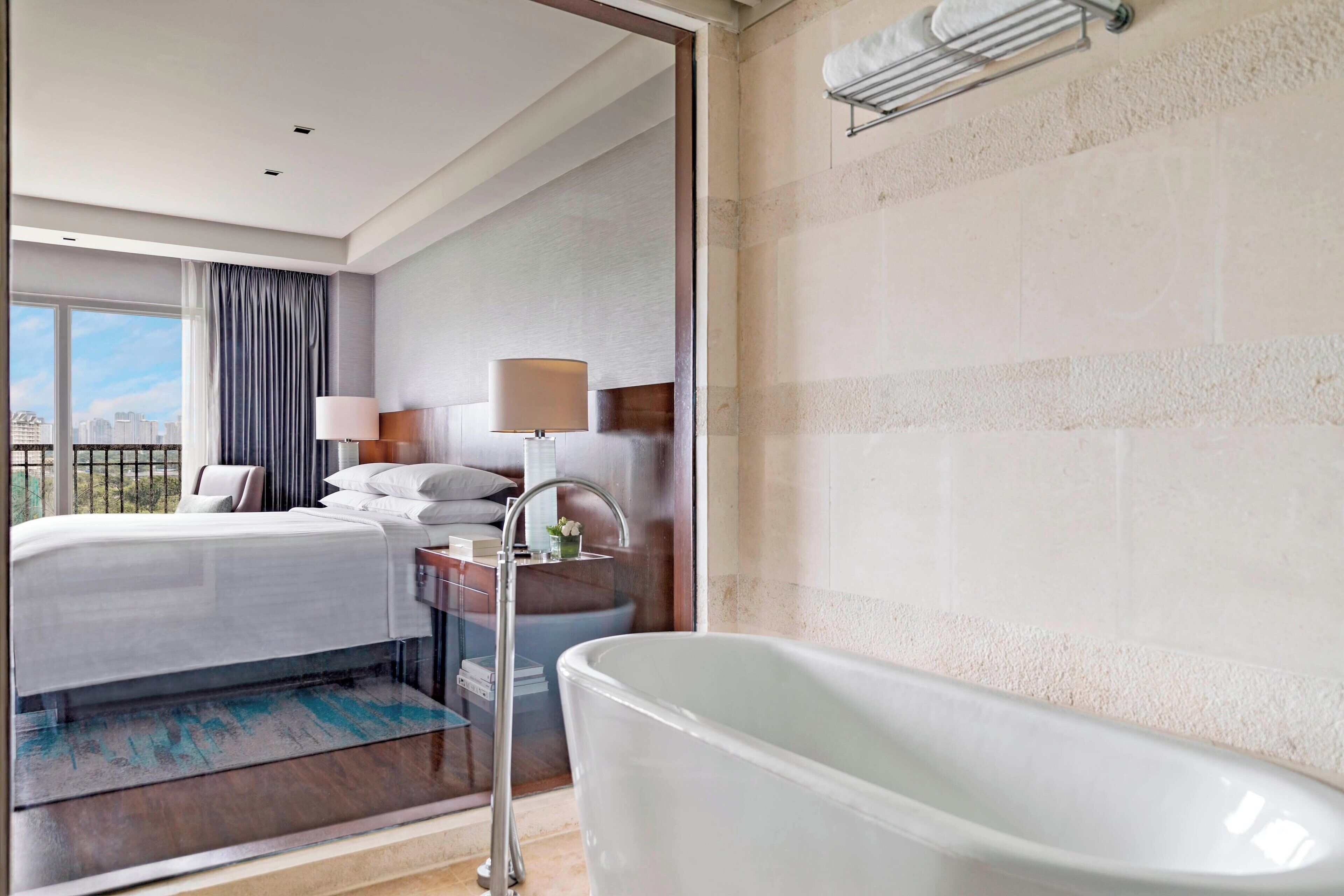 A modern hotel room with a large bed, a bathtub, and a city view.