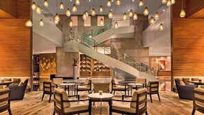 Eine großzügige Lobby mit mehreren Sitzbereichen, einer zentralen Treppe und modernen Leuchten.