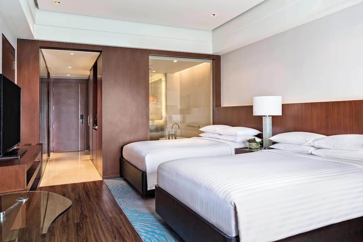 A hotel room with two beds, a TV, a desk, and a bathroom visible through an open door.