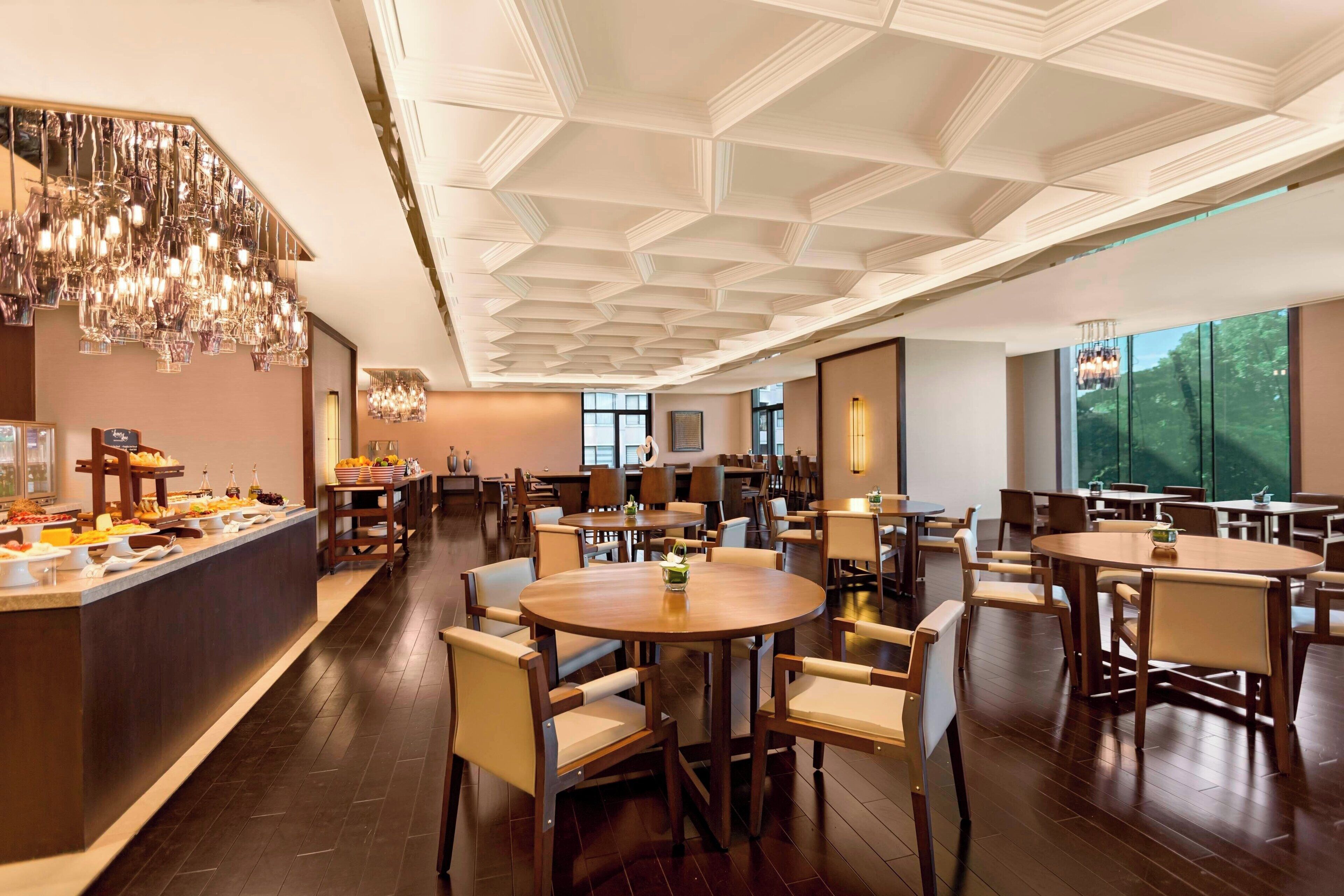 A hotel dining area with round tables, chairs, a buffet counter, and a decorative ceiling.