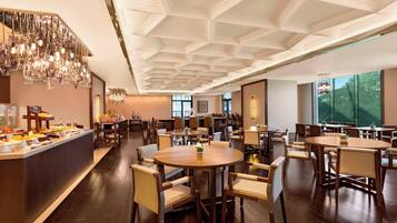 A hotel dining area with round tables, chairs, a buffet counter, and a decorative ceiling.