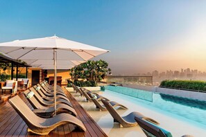 A rooftop pool area with lounge chairs and umbrellas, overlooking a city skyline. - Manila Marriott Hotel at Newport World Resorts (Pasay)