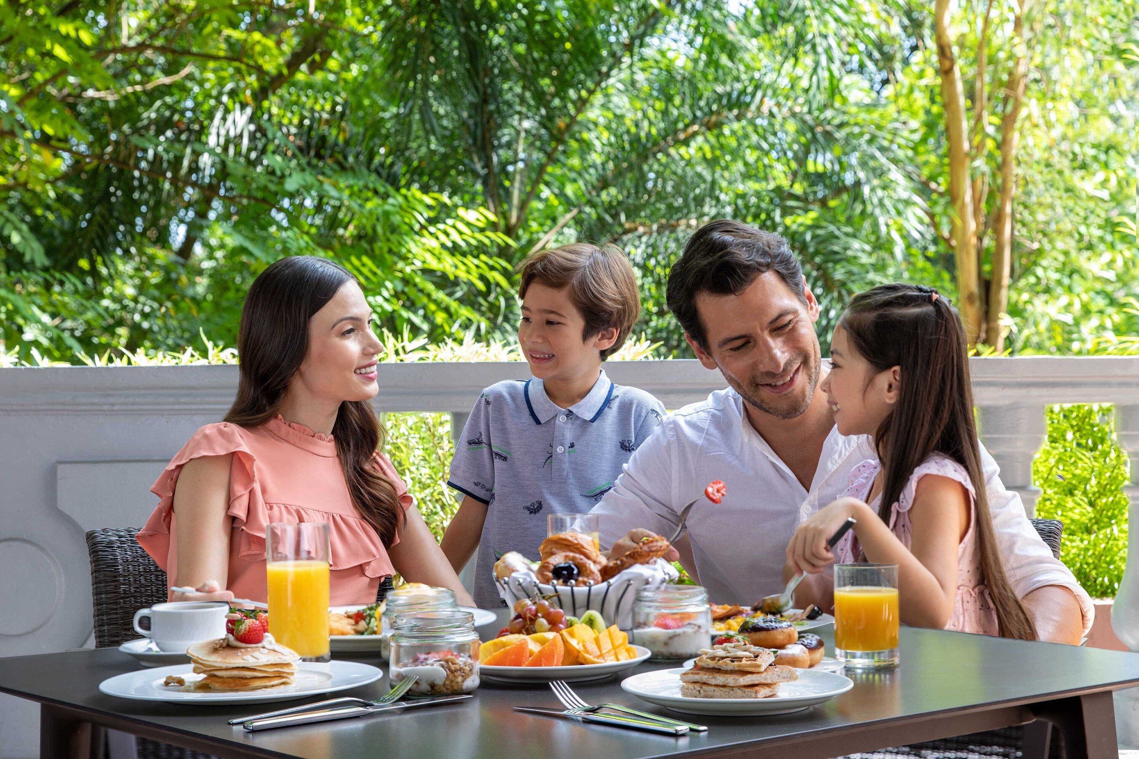 Una familia desayunando al aire libre, con una mesa preparada en medio de abundante vegetación.