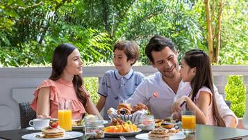 Una familia desayunando al aire libre, con una mesa preparada en medio de abundante vegetación.