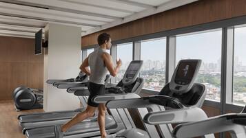 Un gimnasio moderno con cintas de correr, una bicicleta estática y un amplio ventanal con vistas a la ciudad.