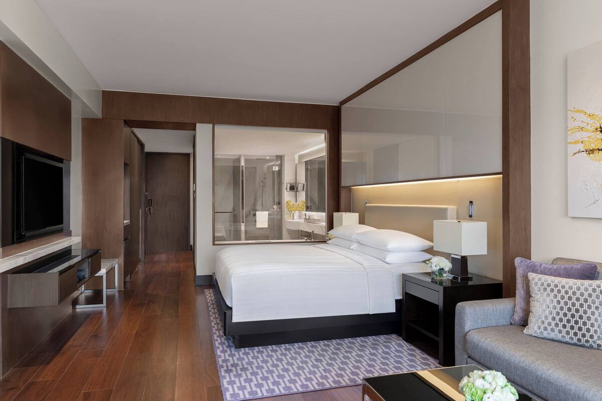 A modern hotel room with a large bed, a TV, a desk, and a sofa.