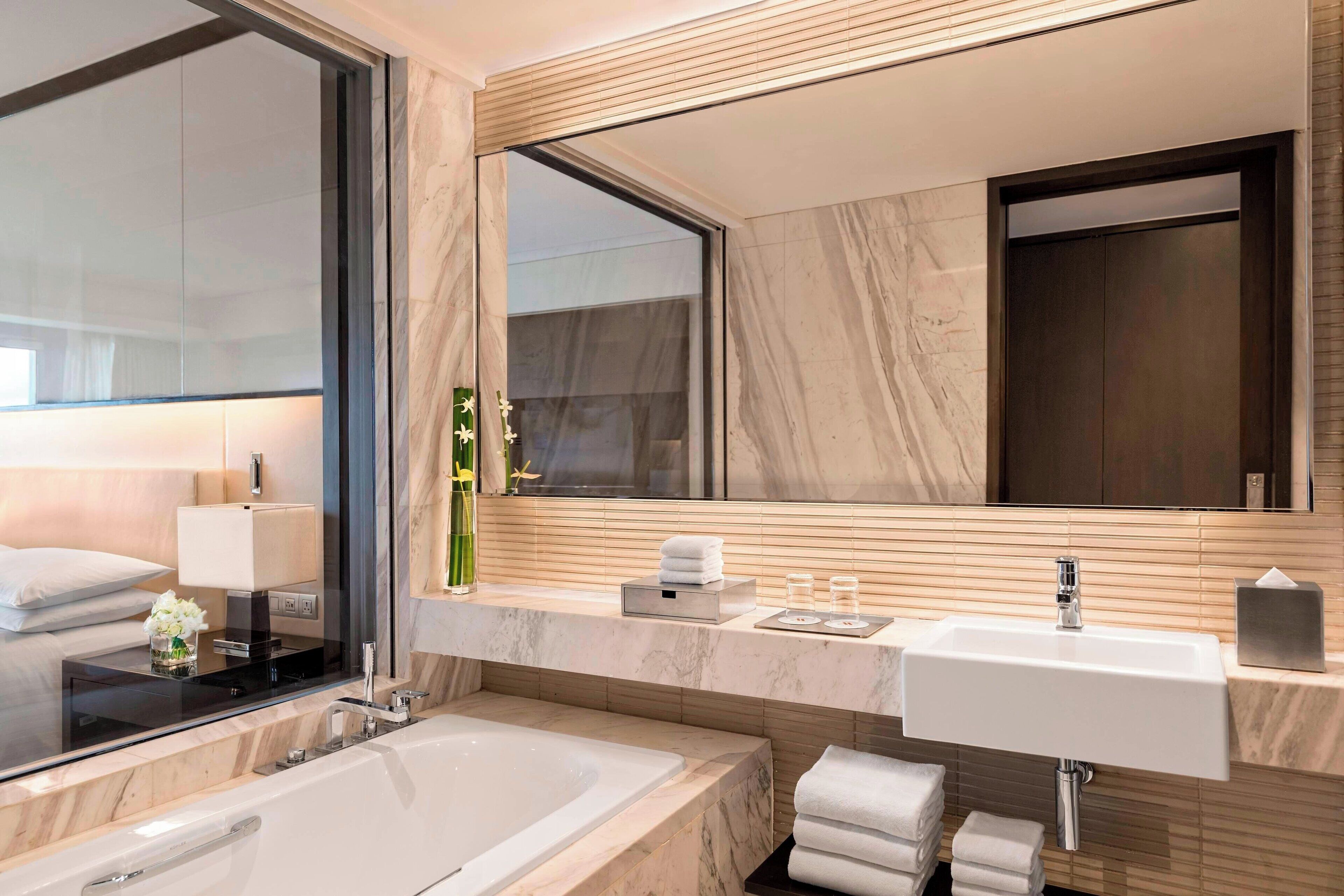 A modern bathroom with a large mirror, a bathtub, a sink, and a vanity with toiletries.