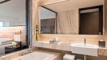 A modern bathroom with a large mirror, a bathtub, a sink, and a vanity with toiletries.