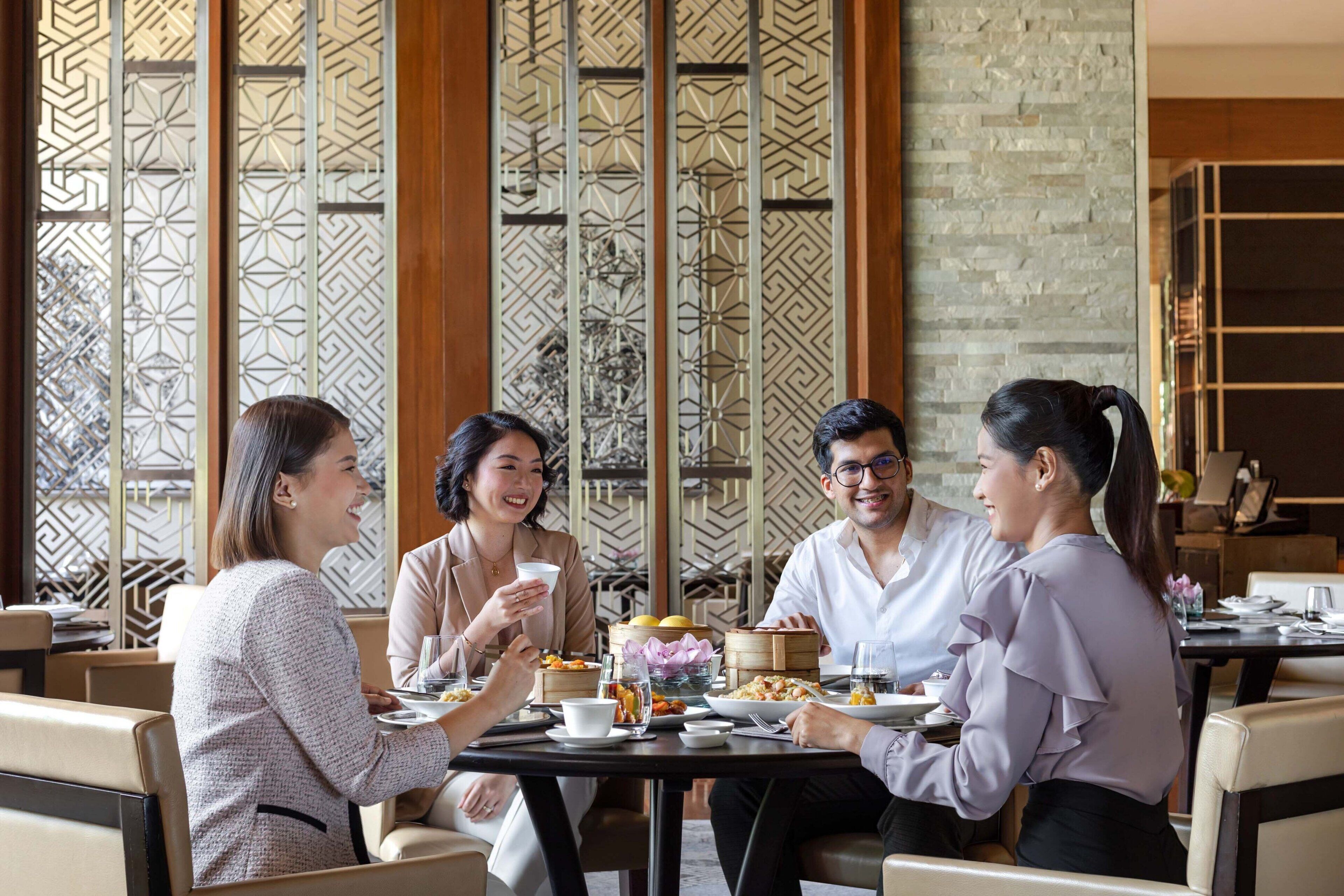 A group of people dining at a table in a restaurant with a decorative wall and wooden panels in the background.