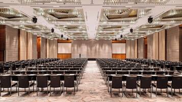 Un salón de conferencias con filas de mesas y sillas, una alfombra estampada y candelabros decorados.