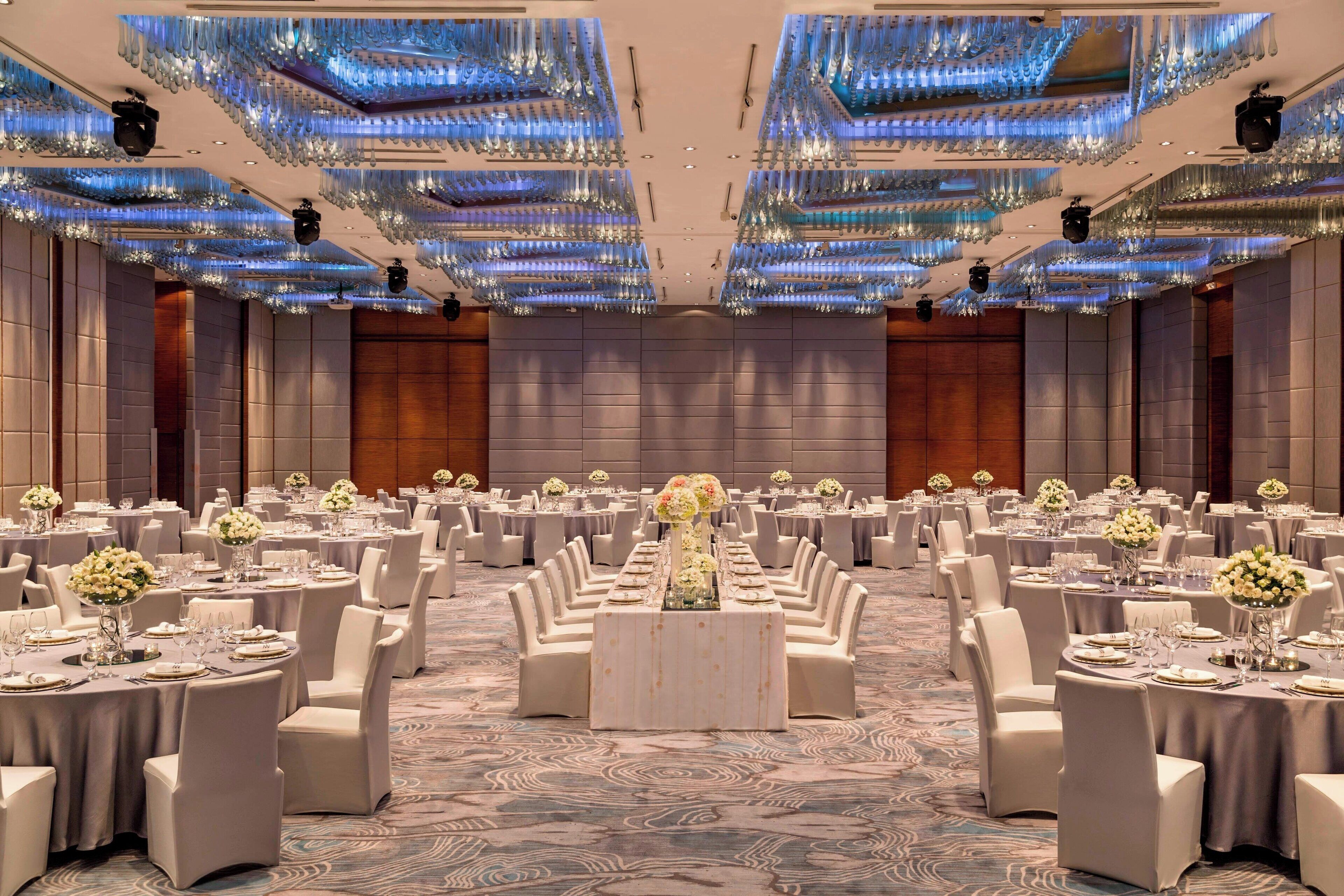 A banquet hall with round tables, white chairs, and floral centerpieces.