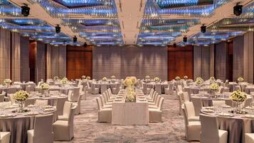 A banquet hall with round tables, white chairs, and floral centerpieces.