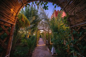 Un sentier bordé d’une arche en bambou, entouré d’une végétation luxuriante et ponctué d’escaliers en pierre.