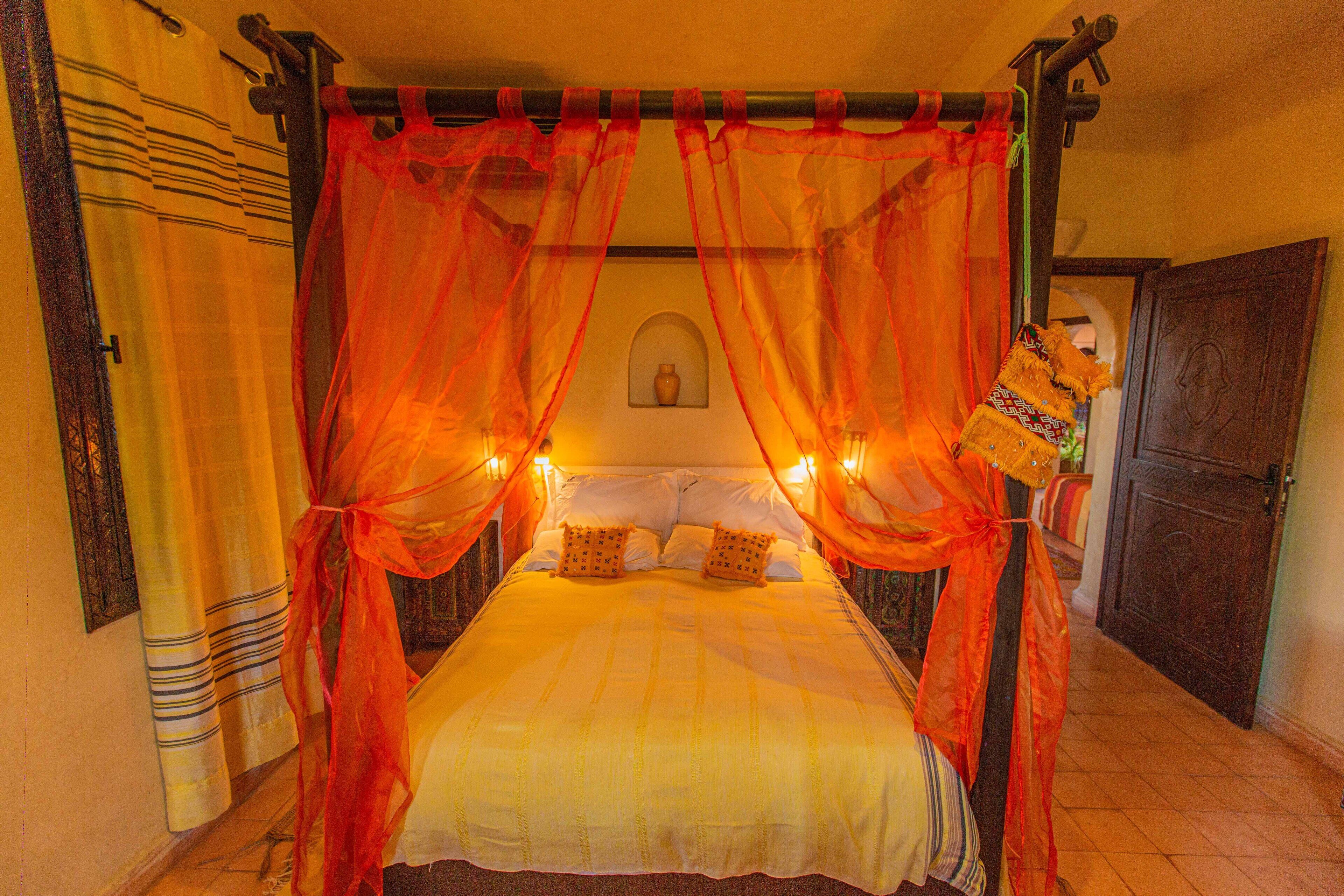 Una cama con dosel, un jarrón fijado a la pared y una puerta con picaporte decorativo.